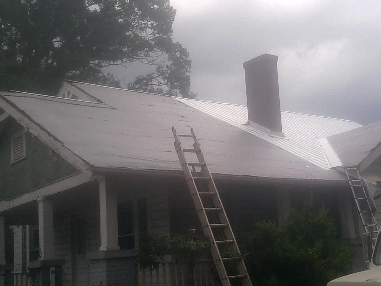 Ladders against a metal roof on an older home with a brick chimney in Hanover